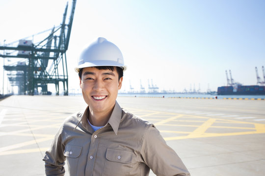 Male shipping industry worker with hands on hips with shipping dock background