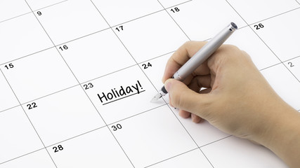 Concept image of calendar with a woman hand writing. Words Holiday written on calendar to remind you an important appoinment.