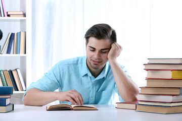 Young man reading book at table in room