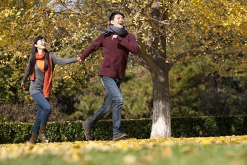 Obraz premium Cheerful young couple in love running on the lawn in autumn