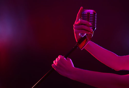 Female hand holding a retro microphone against colourful background