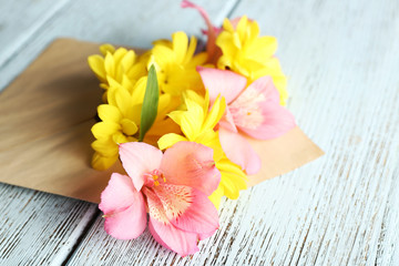 Fototapeta na wymiar Pink alstroemeria and yellow chrysanthemum in envelope on wooden background