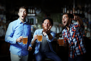 Young men with beer rejoice the victory of their favorite team in the pub