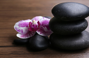 Fototapeta na wymiar Black pebbles with orchid on wooden background