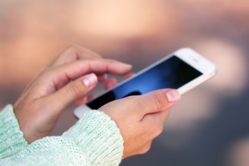 Female hands holding a mobile phone outdoors, on blurred background