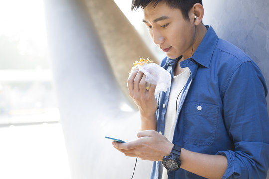 Young man listening to earphones and eating food