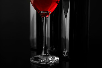 Red wine glass against bottles in a row on black background, close up