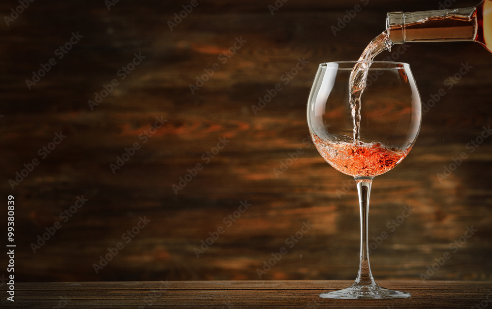 Canvas Prints Rose wine pouring in glass on wooden background