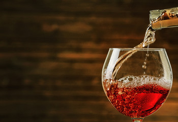 Rose wine pouring in glass on wooden background