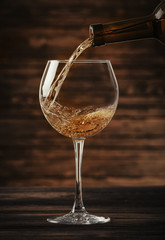 White wine pouring in glass on wooden background