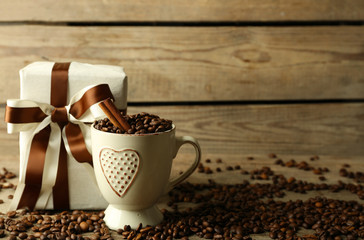 Beautiful gift with bow and coffee grains in mug, on wooden background