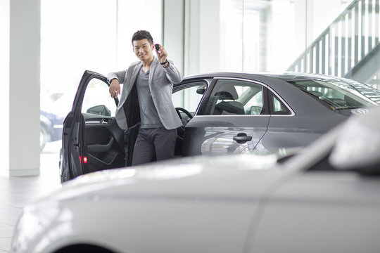 Young Man Buying Car In Showroom