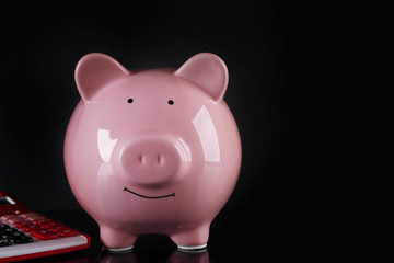 Piggy bank with calculator on dark background
