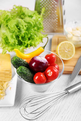 Kitchen utensils and ingredients for salad on table, on light background