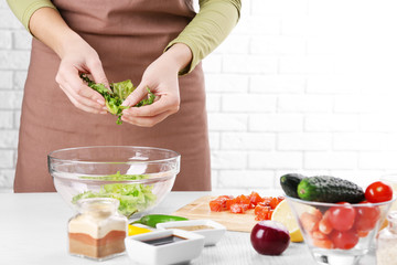 Female hands adding lettuce leaves into bowl with salad, close-up