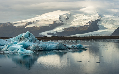 Obrazy na Szkle  Kostka lodu i góra lodowa w lagunie lodowcowej Jokulsarlon na tle śnieżnej góry