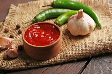Homemade hot sauce and spices on sackcloth, on wooden background