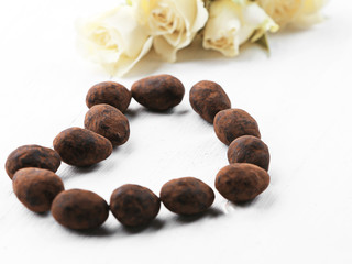 Set of chocolate candies with flowers forming heart on a light wooden background
