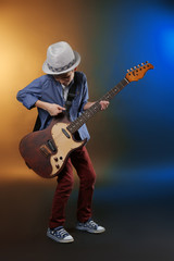 Obraz premium Little boy playing guitar on a dark lighted background