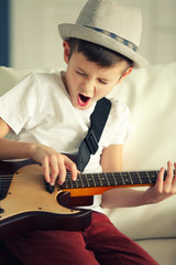 Obraz premium Little boy playing guitar ans singing on a sofa at home, close up