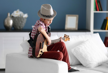 Plakat Little boy playing guitar ans singing on a sofa at home