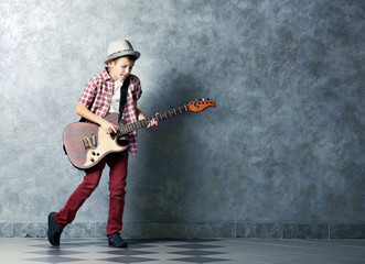 Little boy playing guitar on a grey wall background