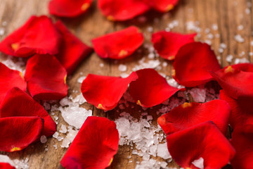 Red roses petals with salt on old wooden board