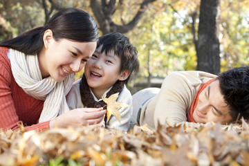 Young family lying on the grass surrounded by Autumn leaves