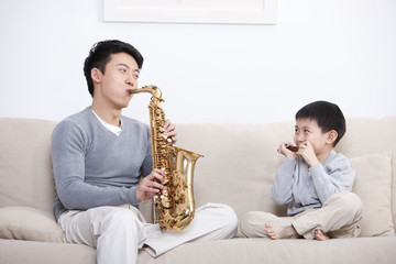 Joyful father and son playing saxophone and harmonica at home