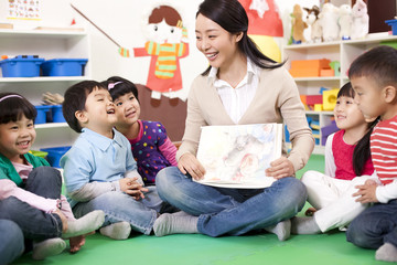 Female teacher showing kindergarten children picture book