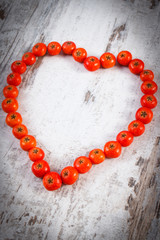 Heart of red autumn rowan on wooden background