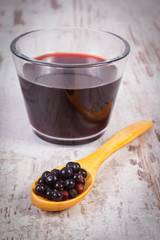 Fresh elderberry on wooden spoon and juice on old wooden background, healthy nutrition