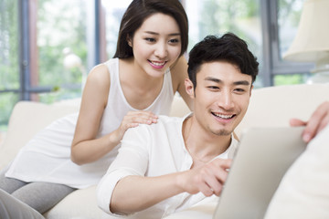 Cheerful young couple using digital tablet in living room