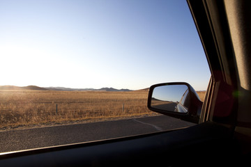 Car sideview mirror with road going through field in the background