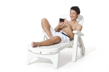 Fototapeta na wymiar Young man using mobile phone on sand chair
