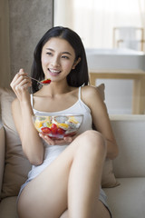 Smiling young woman having salad at home