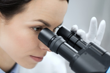 close up of scientist looking to microscope in lab