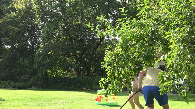 Playful couple boy and girl lifestyle in sunny hot summer day. Man guy catch and spray woman girl in underwear with water hose in garden yard. Static shot. 4K

