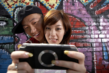 Teenage Boy And Girl Playing On A Game Console In Front Of A Wall Of Graffiti © Blue Jean Images