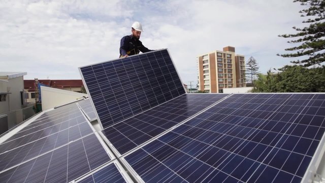 Solar technician installing solar panels on house roof.