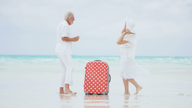 Senior Caucasian couple on a Caribbean beach with a camera and suitcase