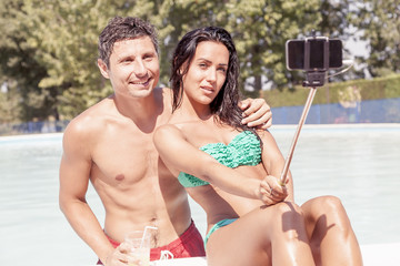 Naklejka premium smiling beautiful couple takes a selfie with smart phone poolsid