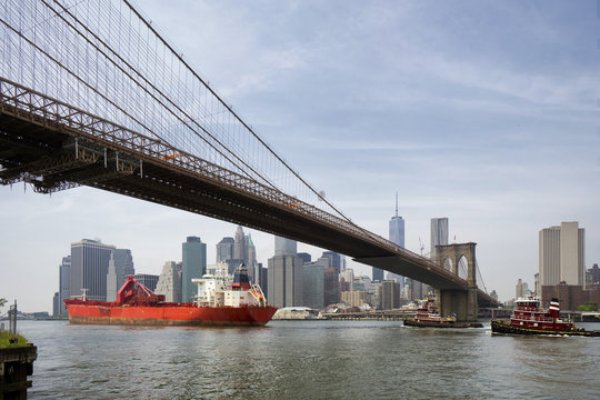 Cargo Ship And Tug Boat Under Brooklyn Bridge, New York City