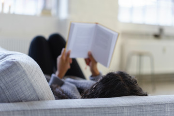 frau liegt entspannt auf dem sofa und liest ein buch