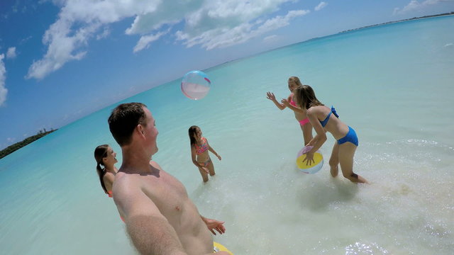 Social media selfie of Caucasian parents and daughters playing beach ball 