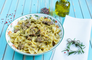 Delicious Italian pasta farfalle with grilled turkey, pesto, herbs in plate served with rosemary sprig on white napkin, red and black pepper, olive oil in glass bottles over turquoise background