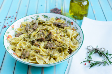 Delicious Italian pasta farfalle with grilled turkey, pesto, herbs in plate served with rosemary sprig on white napkin, red and black pepper, olive oil in glass bottles over turquoise background