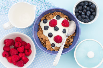 A breakfast table with bran flake cereal, raspberries, blueberries and natural yoghurt. A view from above. 