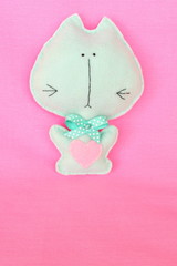     Felt cat - handmade felt green cat with red heart on pink background, hand-stitched toy, a craft out of felt 
