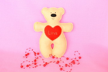 Handmade felt bear - beige felt bear on pink background, hand-stitched toy, a craft out of felt 
